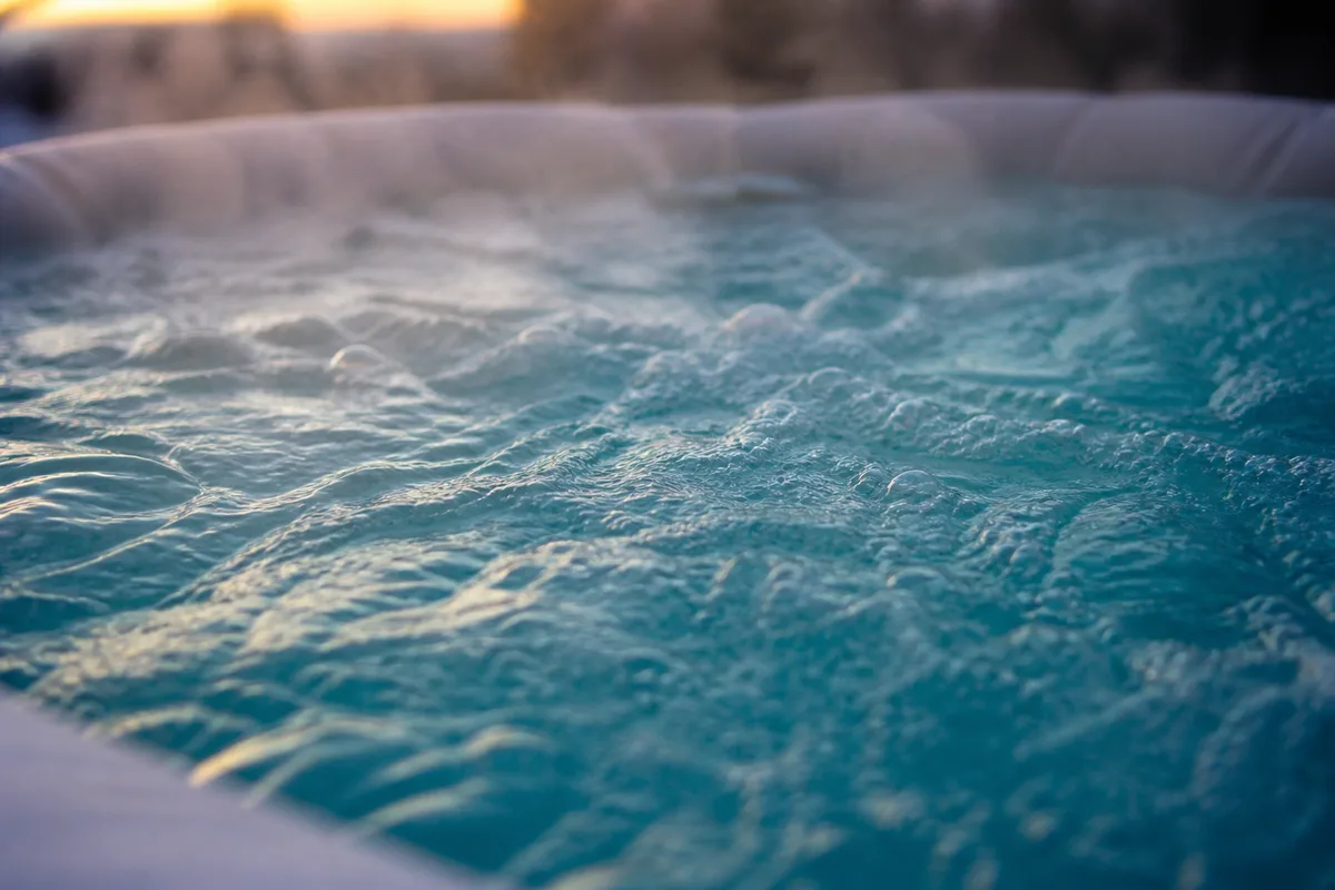 Vue rapprochée de l’eau bouillonnante d’un spa extérieur en fin de journée, vapeur légère au-dessus de la surface