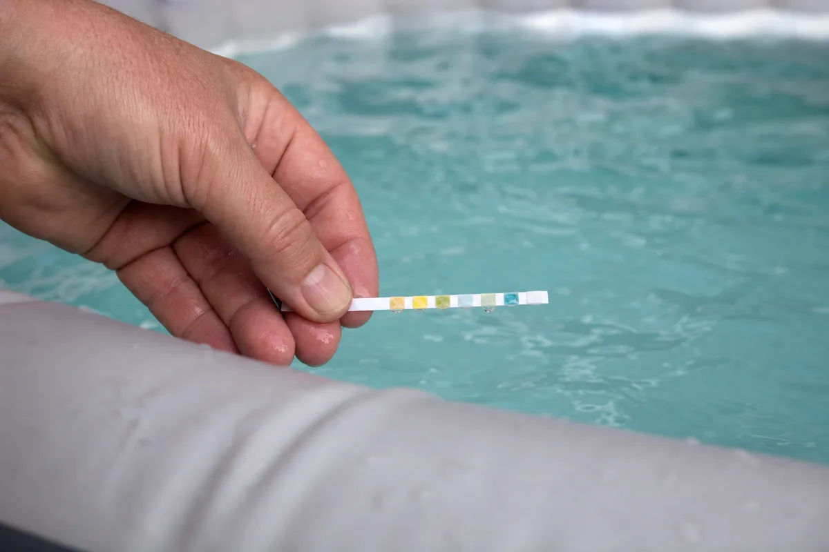 Bandelette de test plongée dans l&rsquo;eau turquoise d&rsquo;un spa gonflable extérieur, mesure du pH