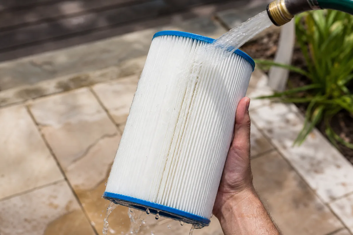 Filtre à cartouche d&rsquo;un spa gonflable rincé au tuyau d&rsquo;arrosage sur une terrasse